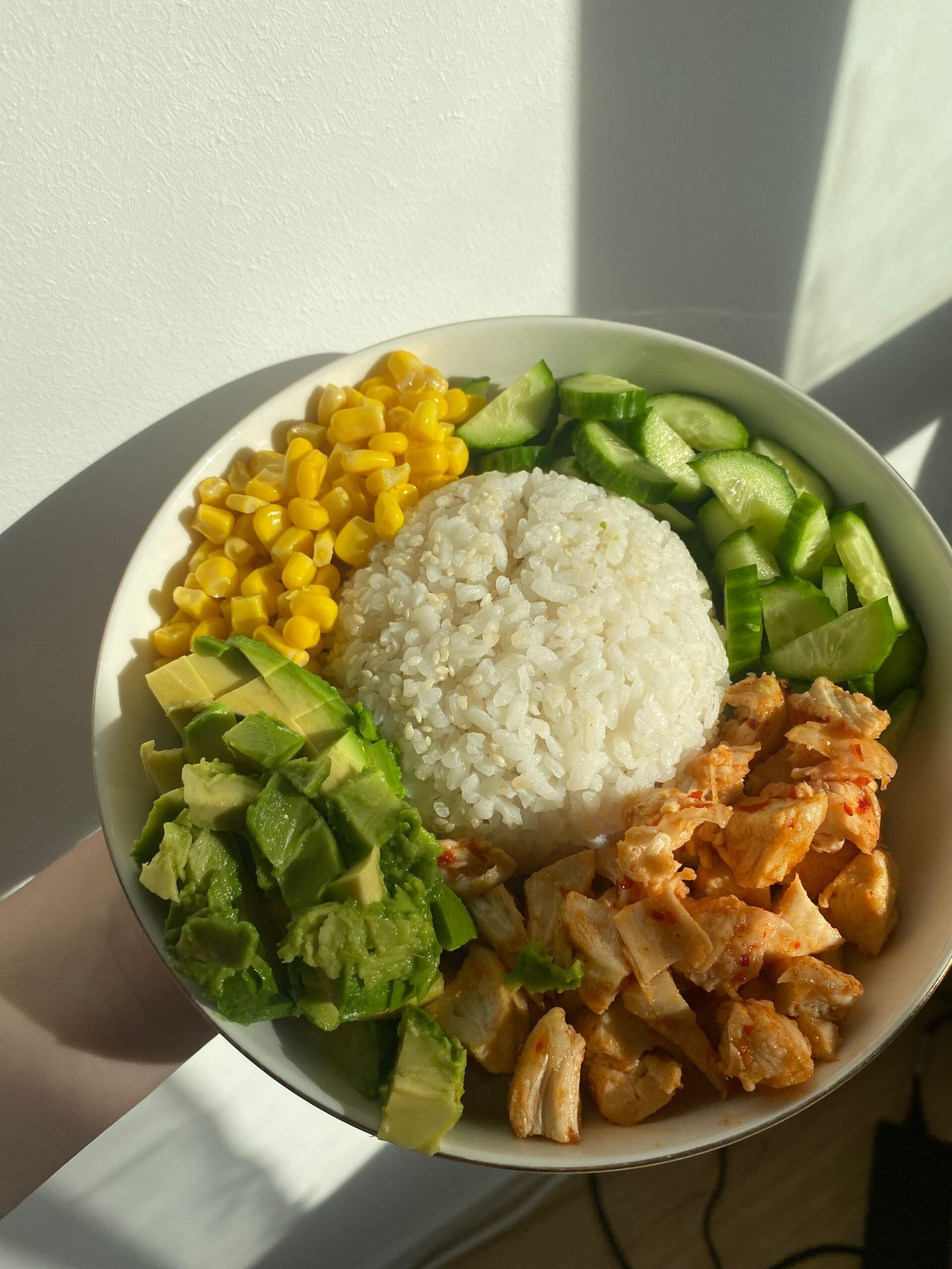 Chicken and rice bowl with corn, avocado, cucumber, and cooked chicken
