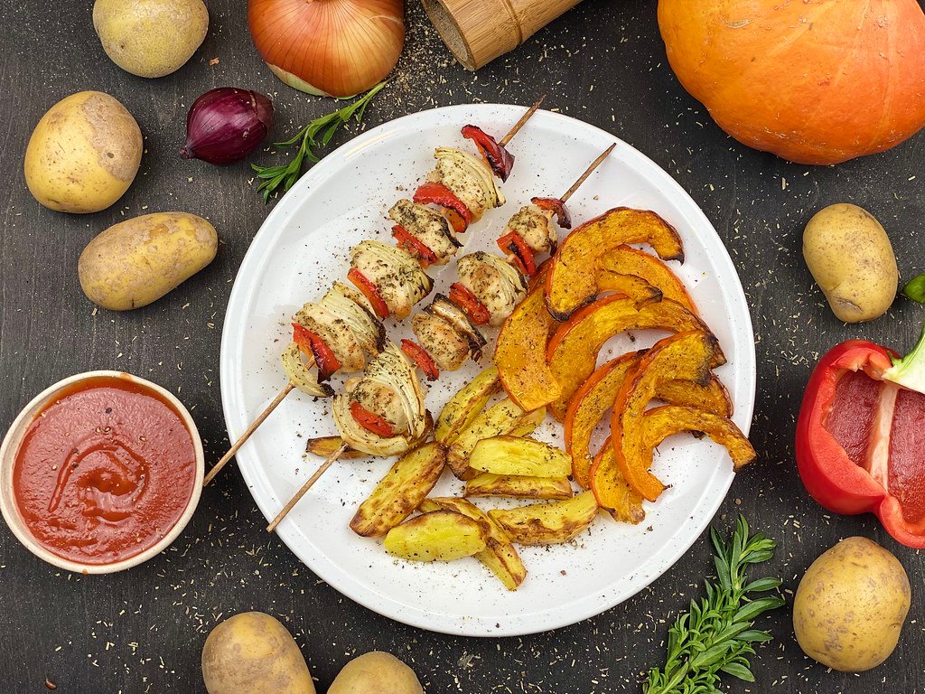 Air fryer-style chicken and vegetable skewers with potato wedges and roasted squash on a white plate
