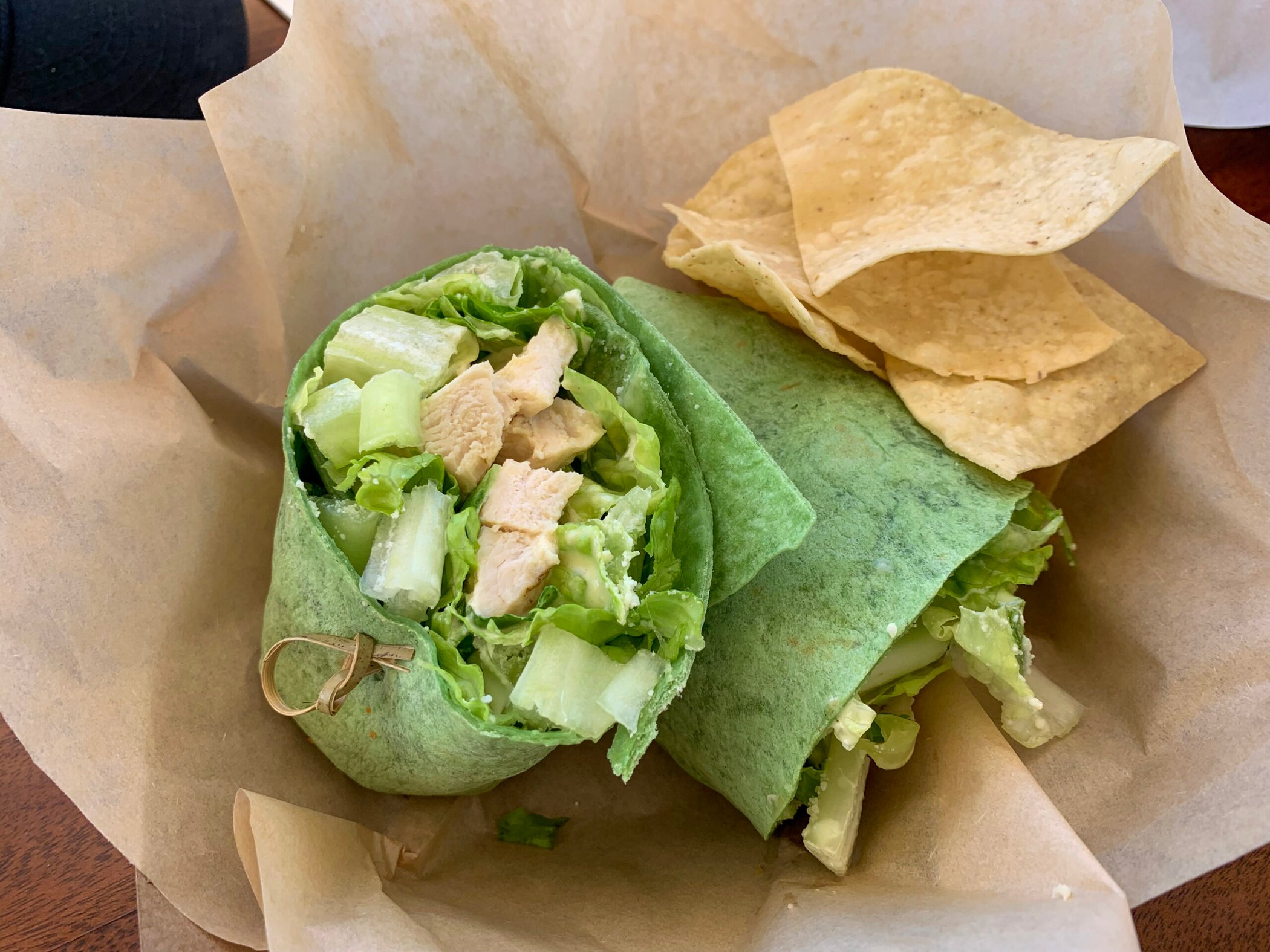 Chicken Caesar spinach wrap with chips on parchment paper