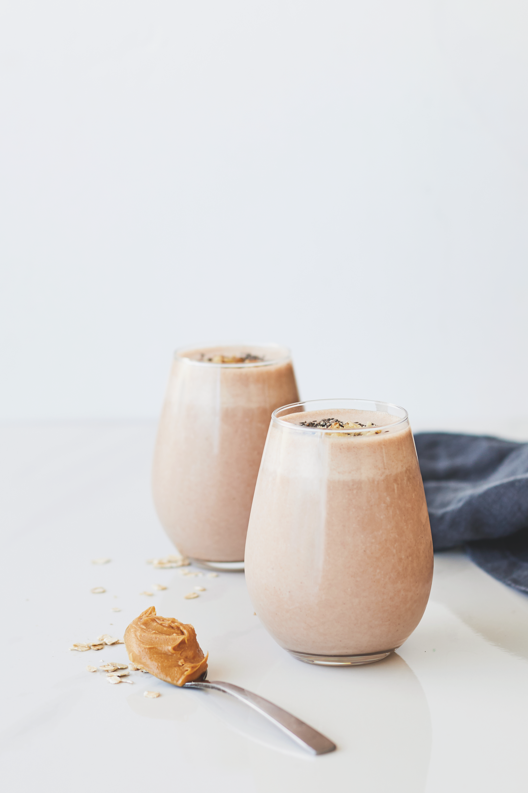 Two thick chocolate protein shakes in glasses with oats and peanut butter